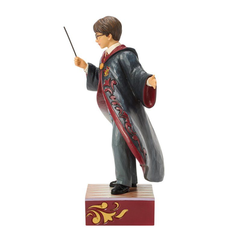 Een Harry Potter-figuurtje in gewaad, met toverstaf in de hand, staand op een doos met een sierlijk gouden ontwerp.