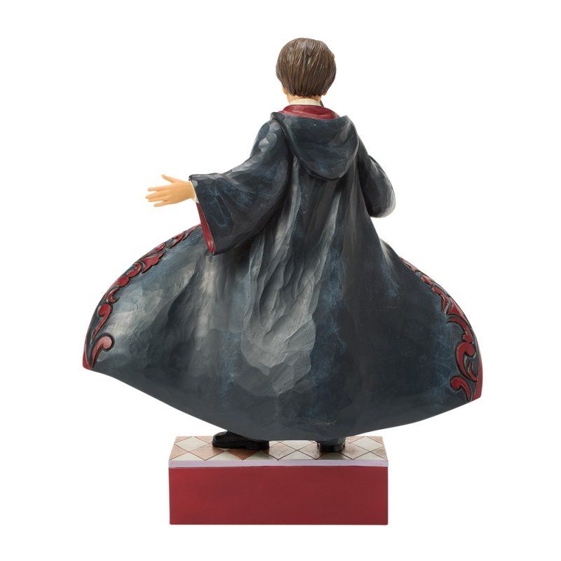 Standbeeld van een figuur in een donker gewaad met rode accenten, met uitgestrekte armen, op een rood-wit platform.