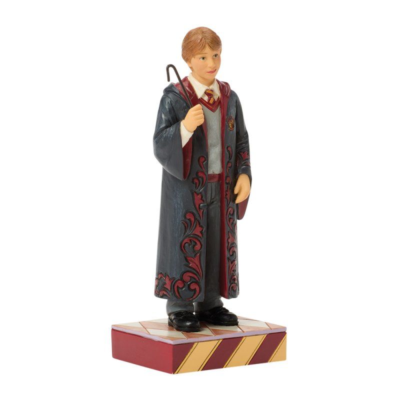 Een beeldje van Ron Weasley in Zweinstein-gewaad, met een toverstaf in zijn hand, staand op een sokkel met patroon.