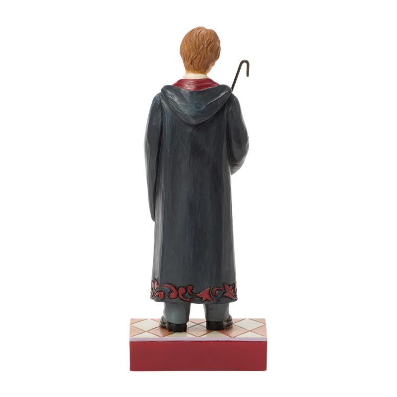 Figuur van een persoon in een donkere mantel, met rood haar, die een wandelstok vasthoudt en op een rood-wit platform staat.