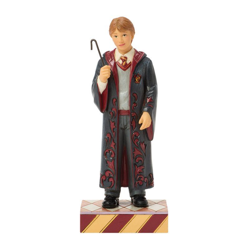 Een beeldje van Ron Weasley in Zweinstein-gewaad, met een toverstaf in zijn hand, staand op een sokkel met patroon.
