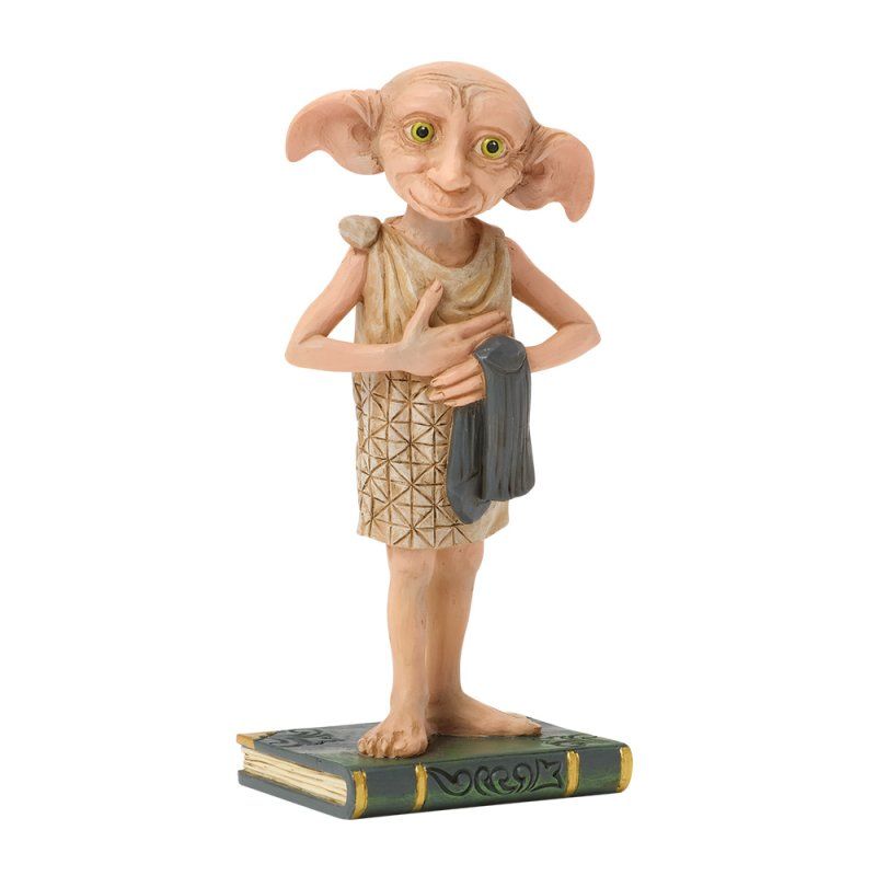 Dobby, een beeldje van een huiself, staat op een boek en houdt een donkere doek vast. Hij heeft een lichtbruine huid, grote oren en groene ogen.