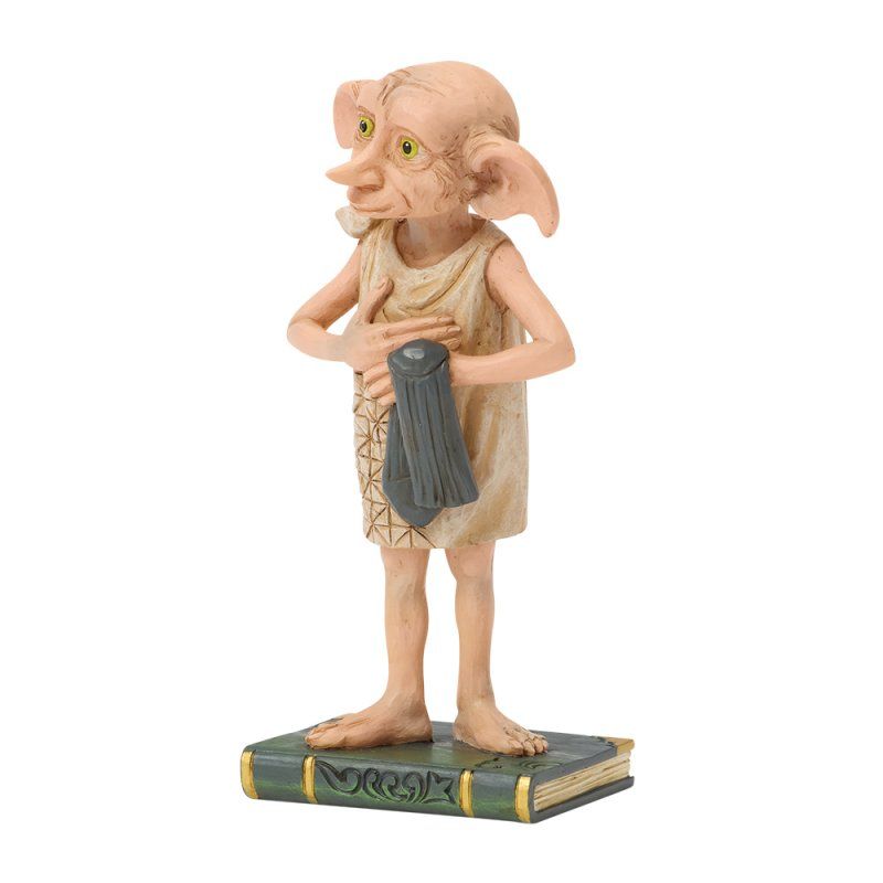 Het beeldje van Dobby de huiself, met een donkergrijs gewaad in zijn handen, staat op een boekvormige sokkel.