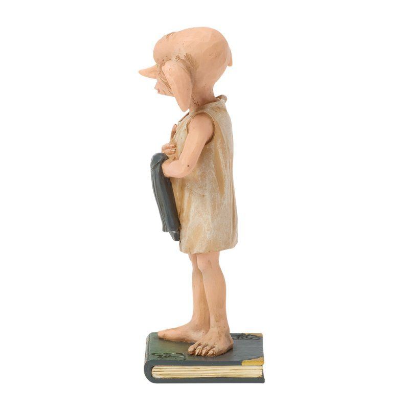 Standbeeld van Dobby, zijaanzicht, staand op een boek, met een donkere doek in zijn hand en beige kleding aan.