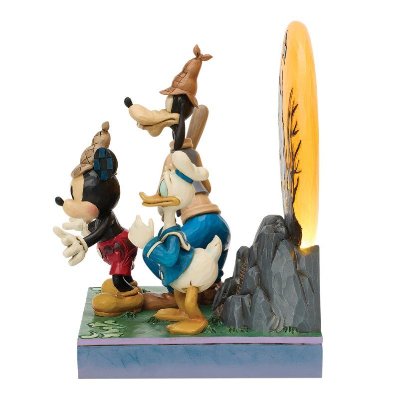 Mickey-, Donald- en Goofy-beeldjes op een stapel, vlakbij een verlichte achtergrond met een bosscène.