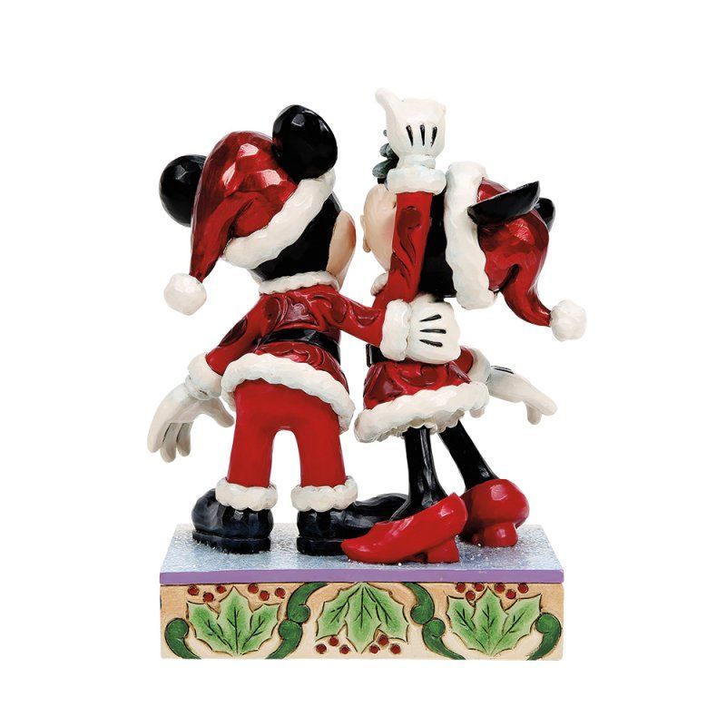 Mickey en Minnie Mouse in kerstmanpakjes die elkaar omarmen. Kerstfiguurtje op een versierde sokkel.