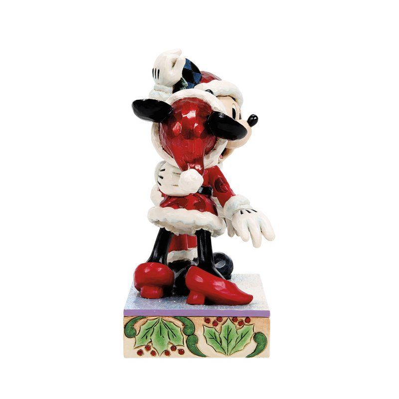 Een beeldje van Minnie Mouse in een kerstmanpak, met een rood kerstornament in haar hand, op een decoratieve sokkel.