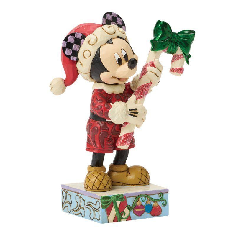 Mickey Mouse in elfenkostuum met een zuurstok met groene strik, op een versierde sokkel.