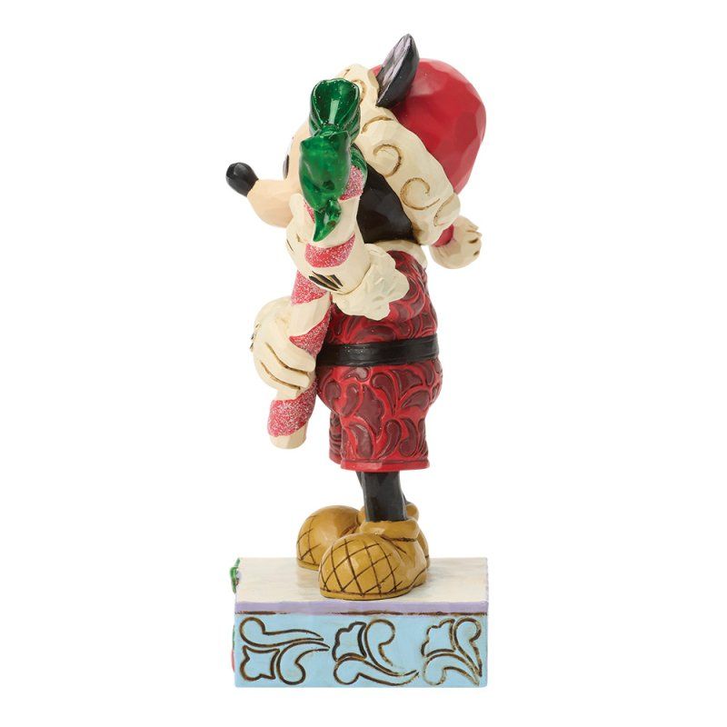 Een kerstfiguurtje van Mickey Mouse met een zuurstok, een kerstmuts en een rood pak, staand op een versierde sokkel.