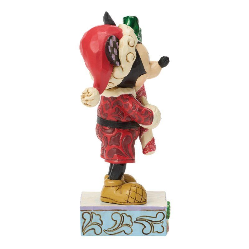 Een Mickey Mouse-figuurtje in kerstmanpak met een zuurstok in zijn hand, staand op een blauwe sokkel met bloemmotieven.