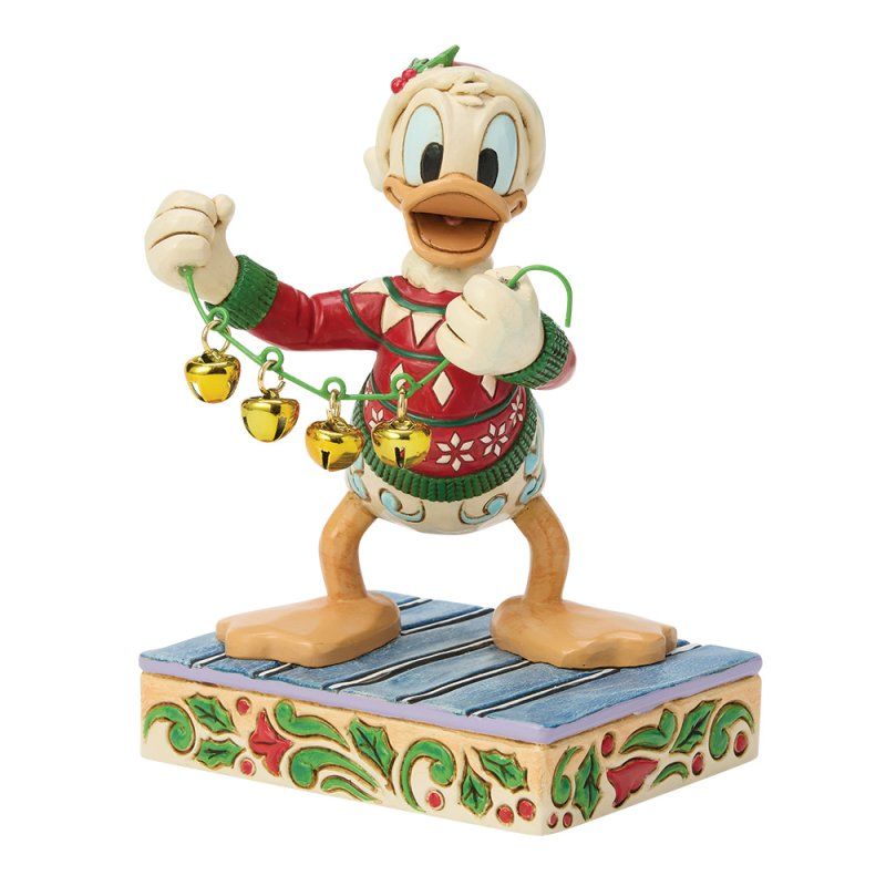 Een Donald Duck-figuurtje in een kersttrui met belletjes op een decoratieve sokkel.