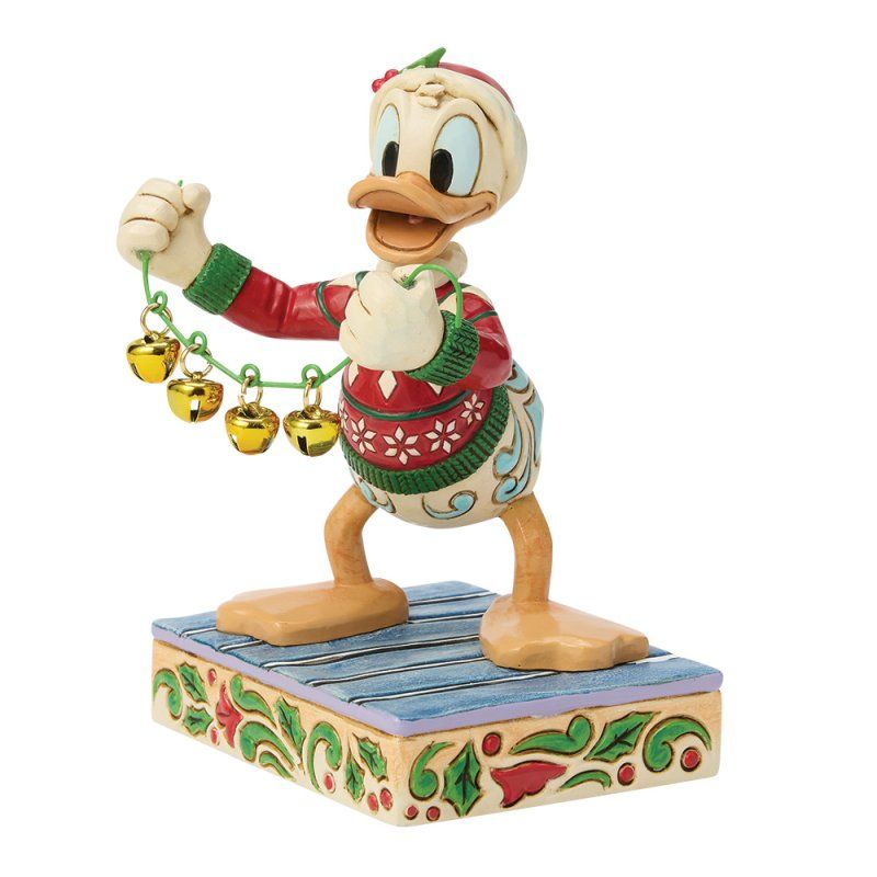 Een Donald Duck-figuurtje in een kersttrui met belletjes op een decoratieve sokkel.