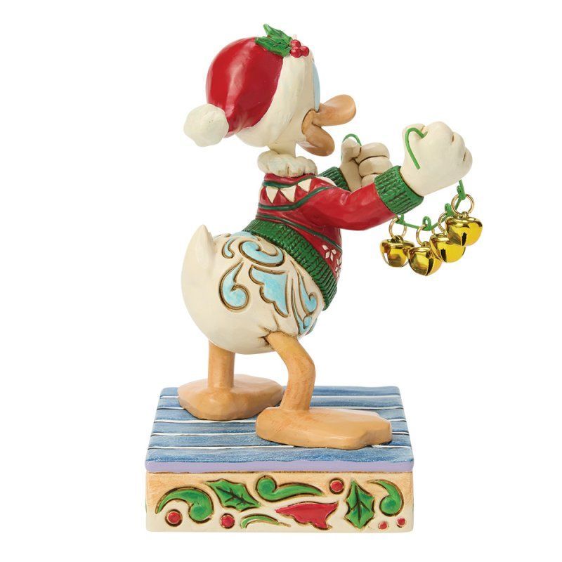 Een Donald Duck-figuurtje in een kersttrui, met belletjes in zijn hand, op een versierde sokkel.
