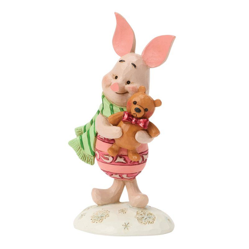 Een beeldje van Knorretje dat een kleine teddybeer vasthoudt, met een groene sjaal en een roze outfit aan, op een besneeuwde achtergrond.