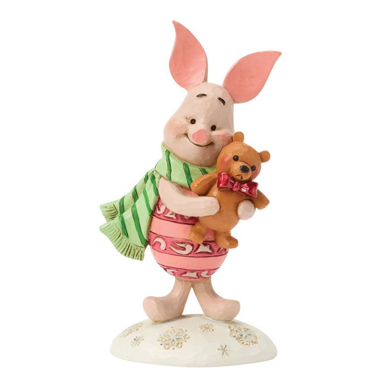Een beeldje van Knorretje met een teddybeer, gekleed in een gestreepte sjaal en een roze jurk, staand op een met sneeuw bedekte sokkel.