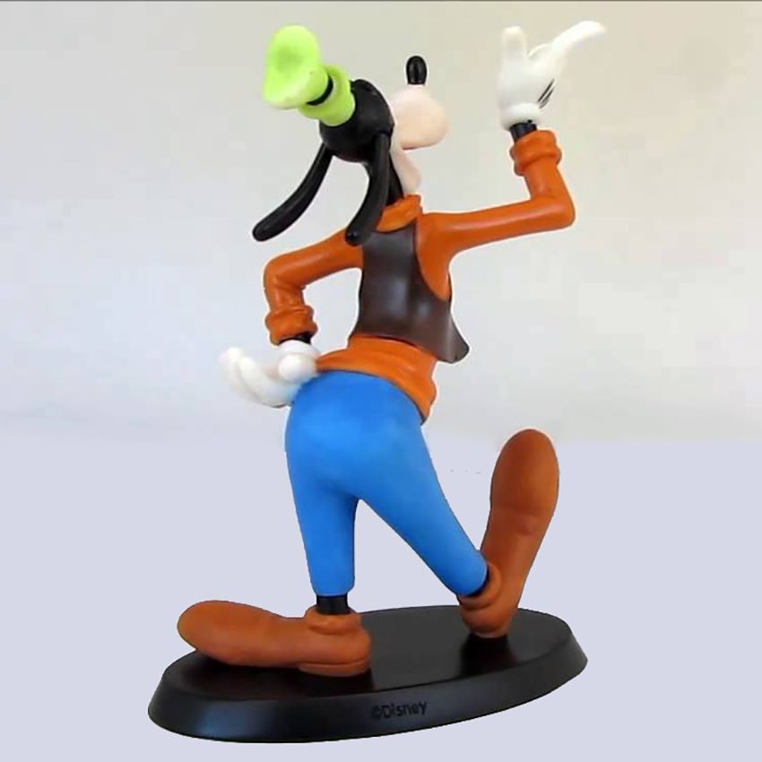 Een grappig figuurtje van achteren gezien, zwaaiend. Hij draagt ​​bruine schoenen, een bruine broek, een vest, een oranje shirt en een groene hoed, en staat op een zwarte sokkel.
