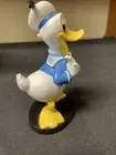 Een Donald Duck-figuurtje in een matrozenpak, staand op een zwarte sokkel.
