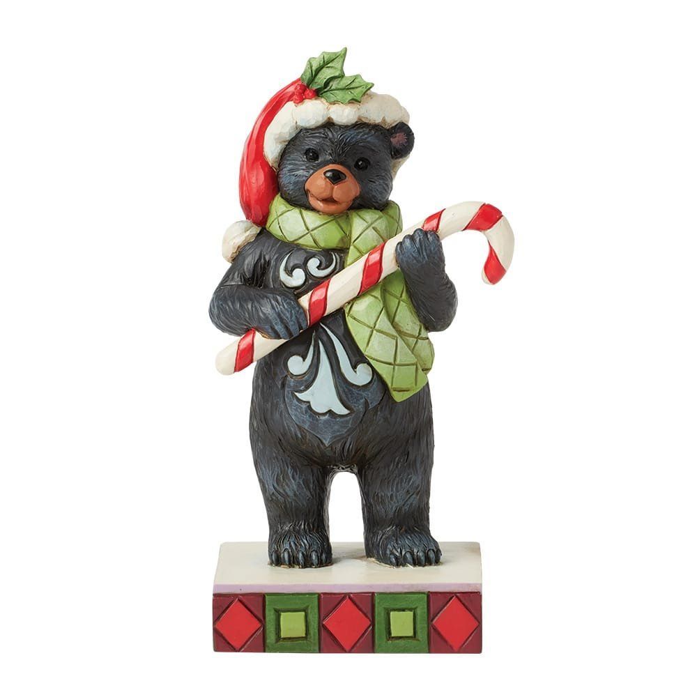 Een beeldje van een zwarte beer met een kerstmuts en -sjaal, die een zuurstok vasthoudt.