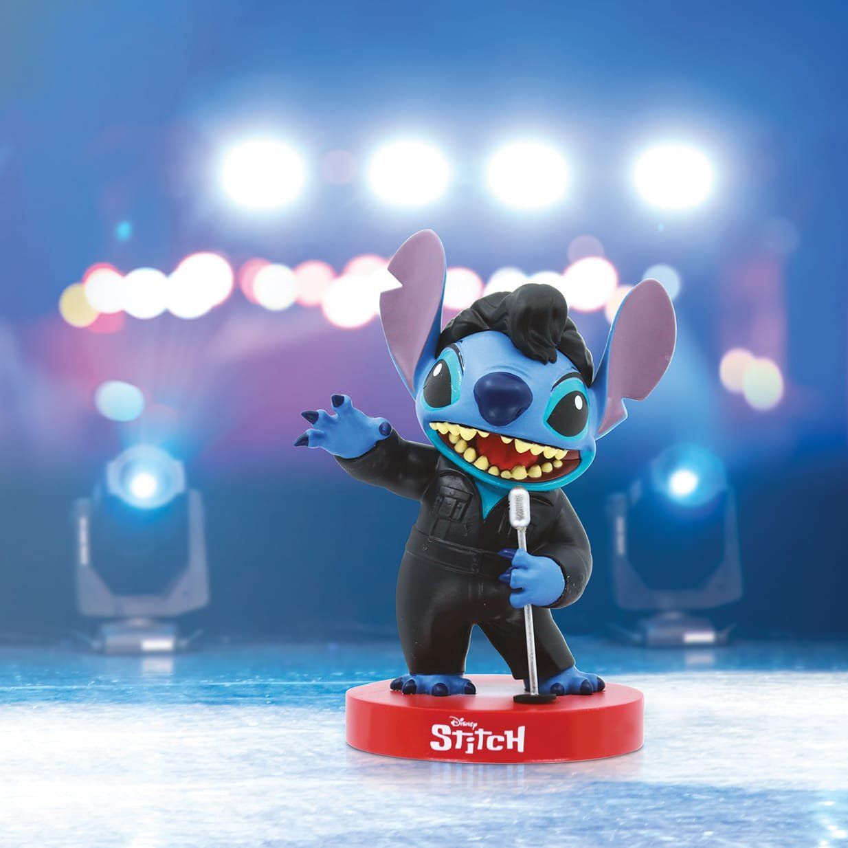 Een Stitch-figuurtje verkleed als zanger, met een microfoon in zijn hand, op een podium met lichtjes.