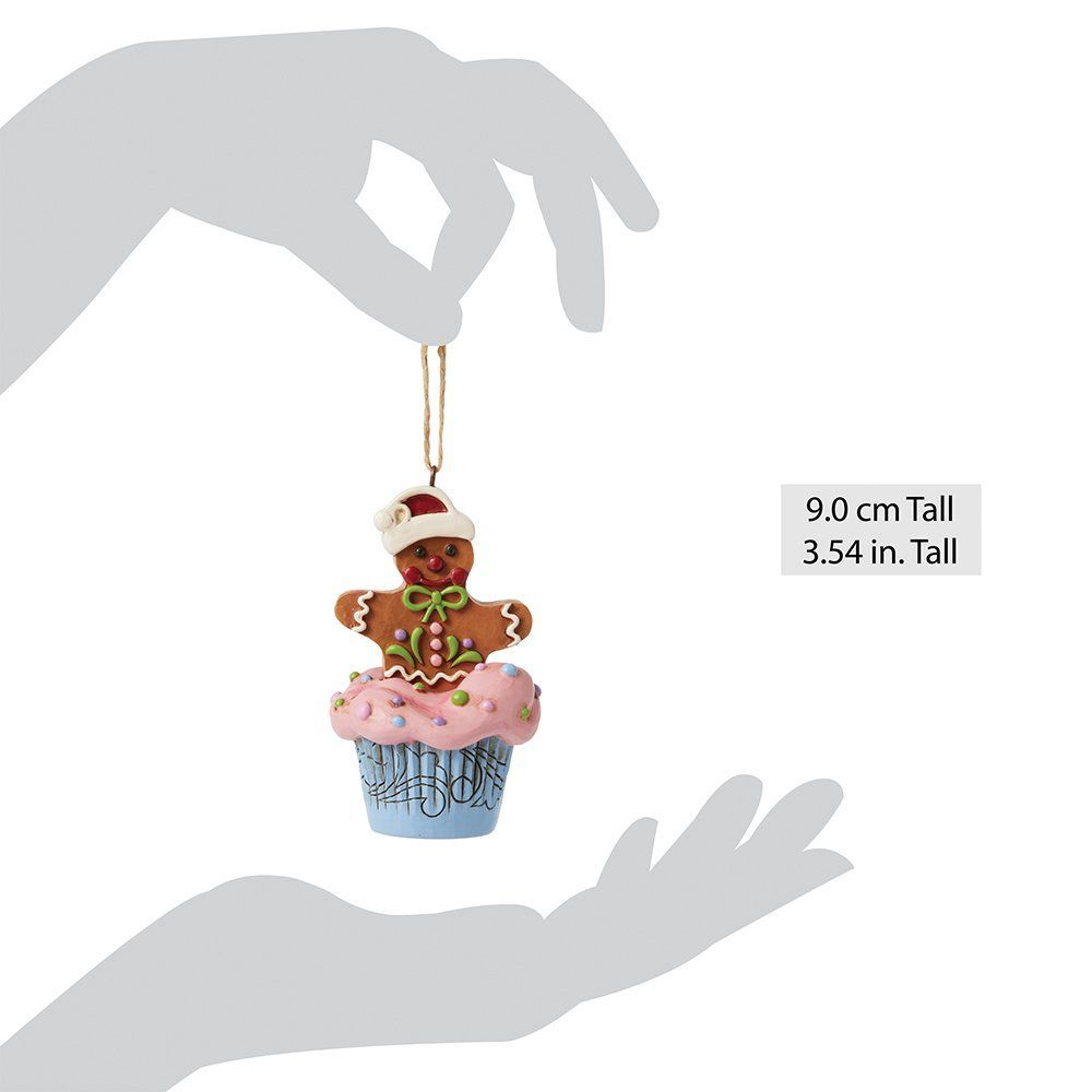 Een kerstornament in de vorm van een peperkoekmannetje op een roze cupcake met glazuur, een blauw cupcakevormpje met muzieknoten en een rode kerstmuts.