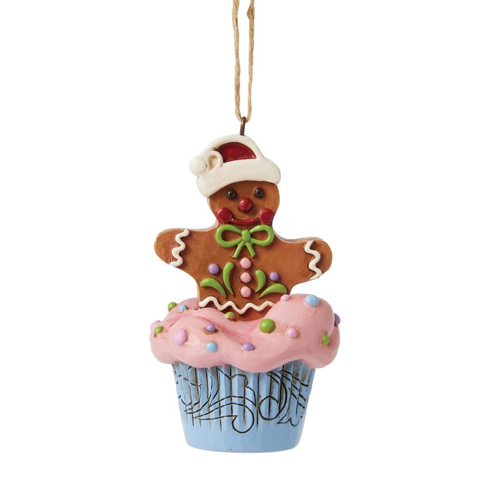 Een kerstornament in de vorm van een peperkoekmannetje op een roze cupcake met glazuur, een blauw cupcakevormpje met muzieknoten en een rode kerstmuts.