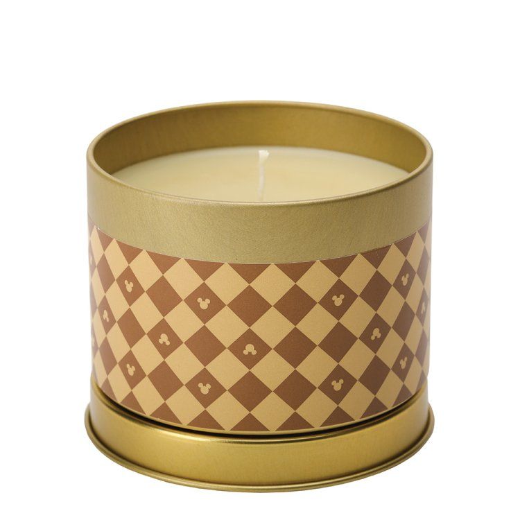 Een kaars in een rond, goudkleurig blikje met een bruin-crème geblokt patroon en een Mickey Mouse-icoontje op elk vakje.