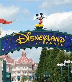 Ingangsbord van Disneyland Parijs met een Mickey Mouse-beeld. Op de achtergrond zijn gebouwen en groene bomen te zien.