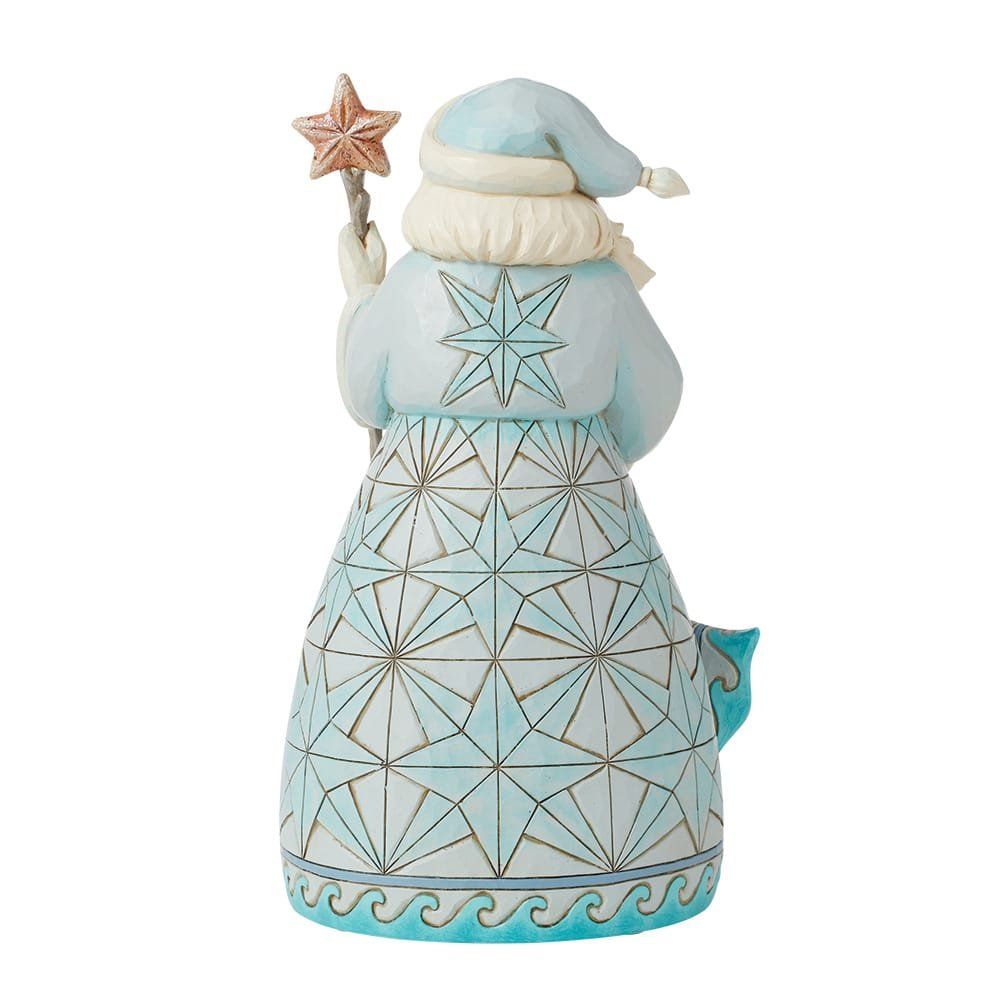 Een kerstmanfiguur aan de kust, in een lichtblauwe mantel met een strandtafereel, met een staf en een kerstkrans.