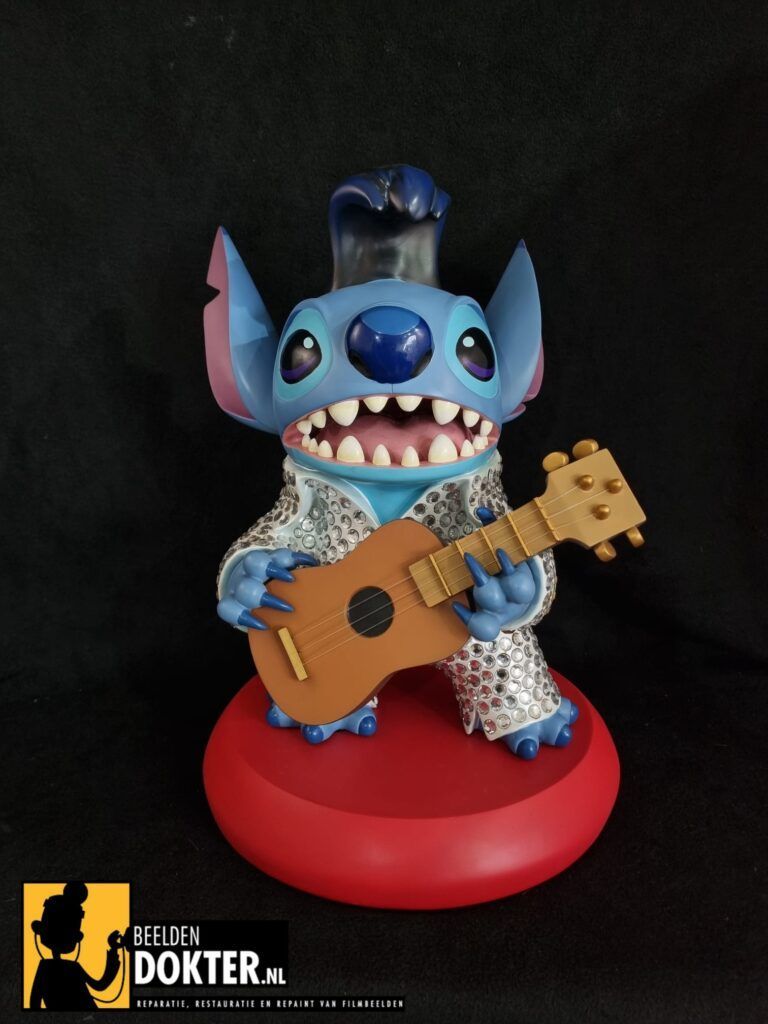 Een Stitch-figuurtje verkleed als Elvis, spelend op een ukelele, op een rode sokkel.