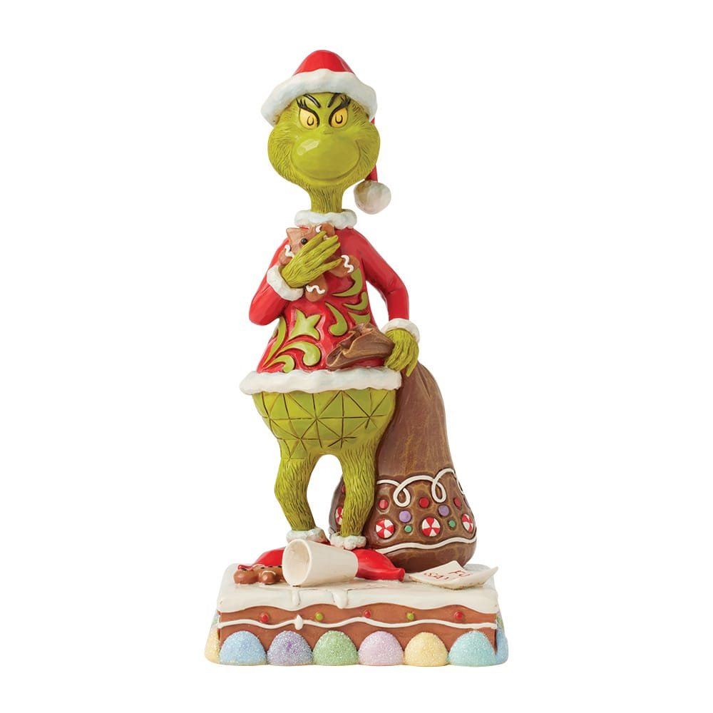 Het Grinch-figuurtje met kerstmuts en rode jas, dat een zak met cadeaus vasthoudt, staat op een versierde taartondergrond.