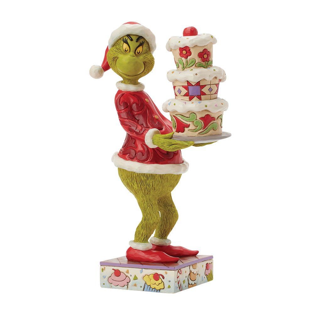 Een standbeeld van de Grinch in een kerstmanpak, met een versierde taart met meerdere lagen.