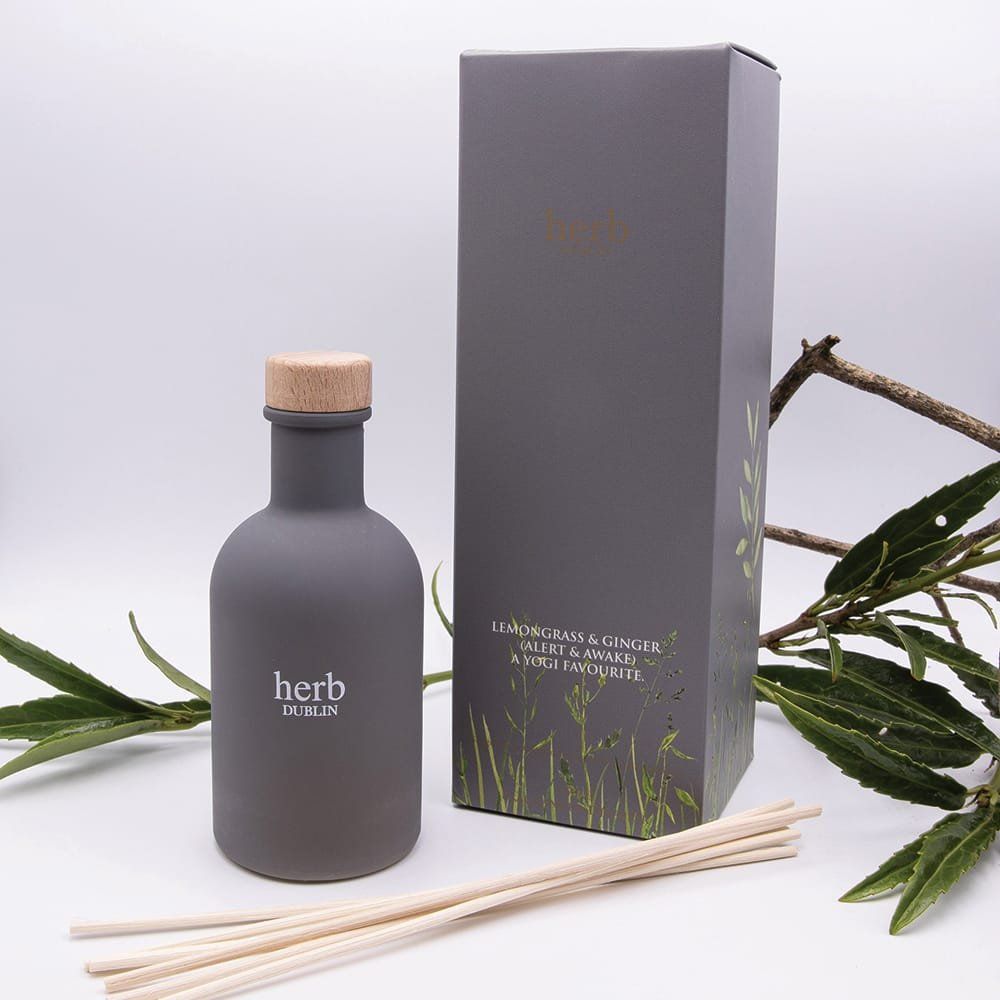 Grijze fles en doos voor een etherische olie diffuser met rietjes op een witte achtergrond, versierd met groen.