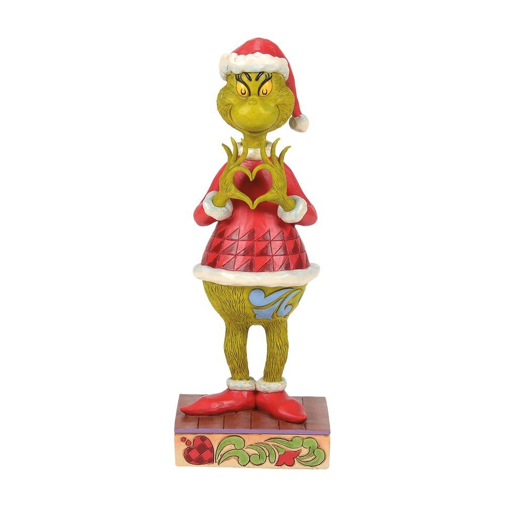 Een Grinch-figuur met een kerstmuts op, die een hartvormig voorwerp vasthoudt, staat op een sokkel met de tekst