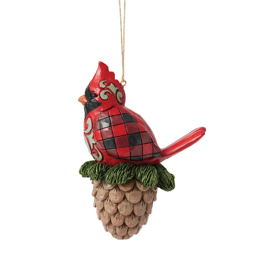 Een rood kardinaalornament, zittend op een dennenappel; met een gouden ophangkoord.