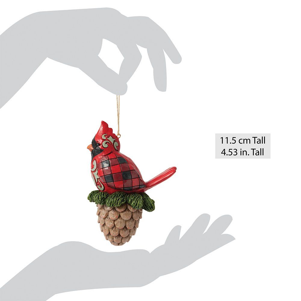 Een rood kardinaalornament, zittend op een dennenappel; met een gouden ophangkoord.