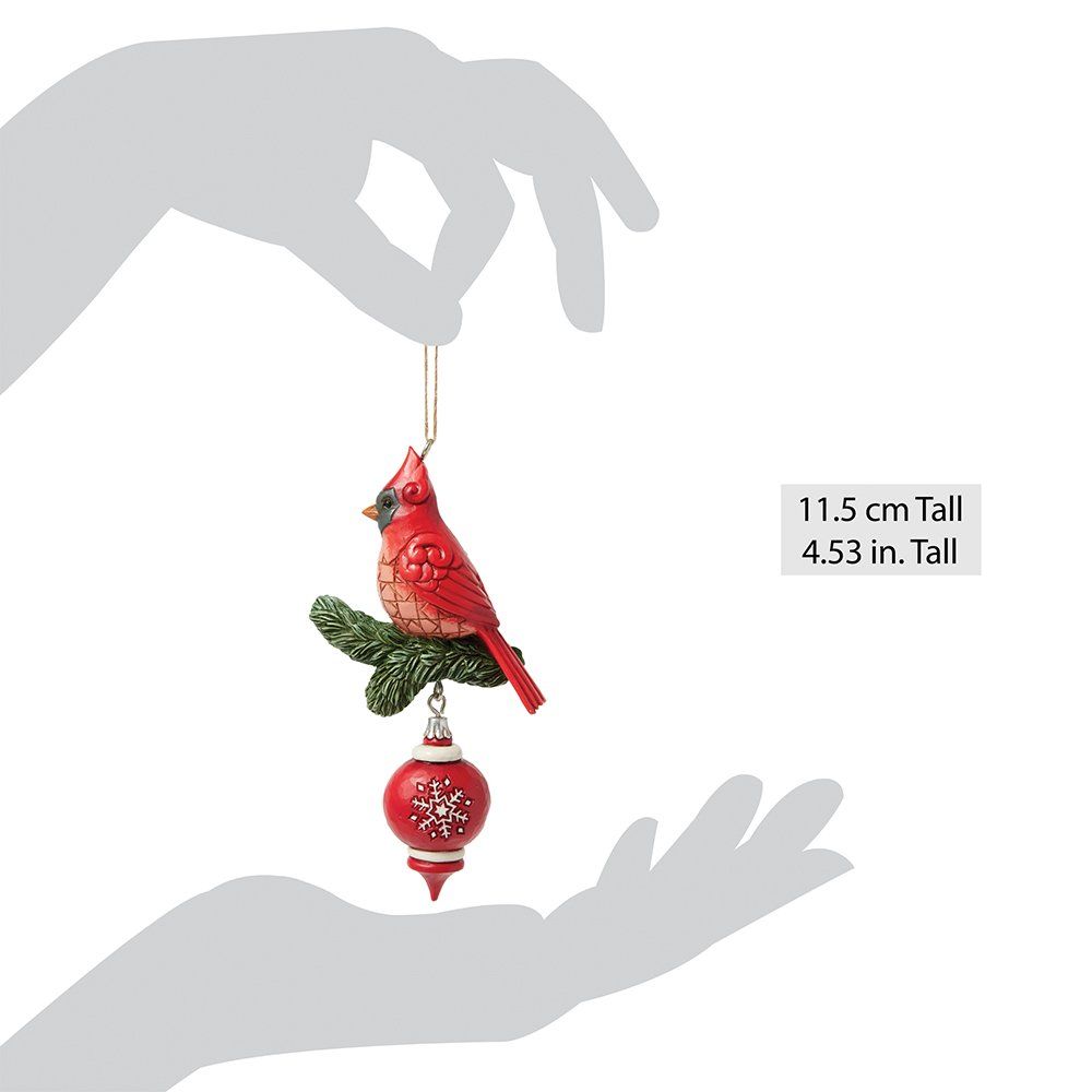 Een kerstornament van een rode kardinaal, zittend op een groene tak boven een rode bal met sneeuwvlokmotief.