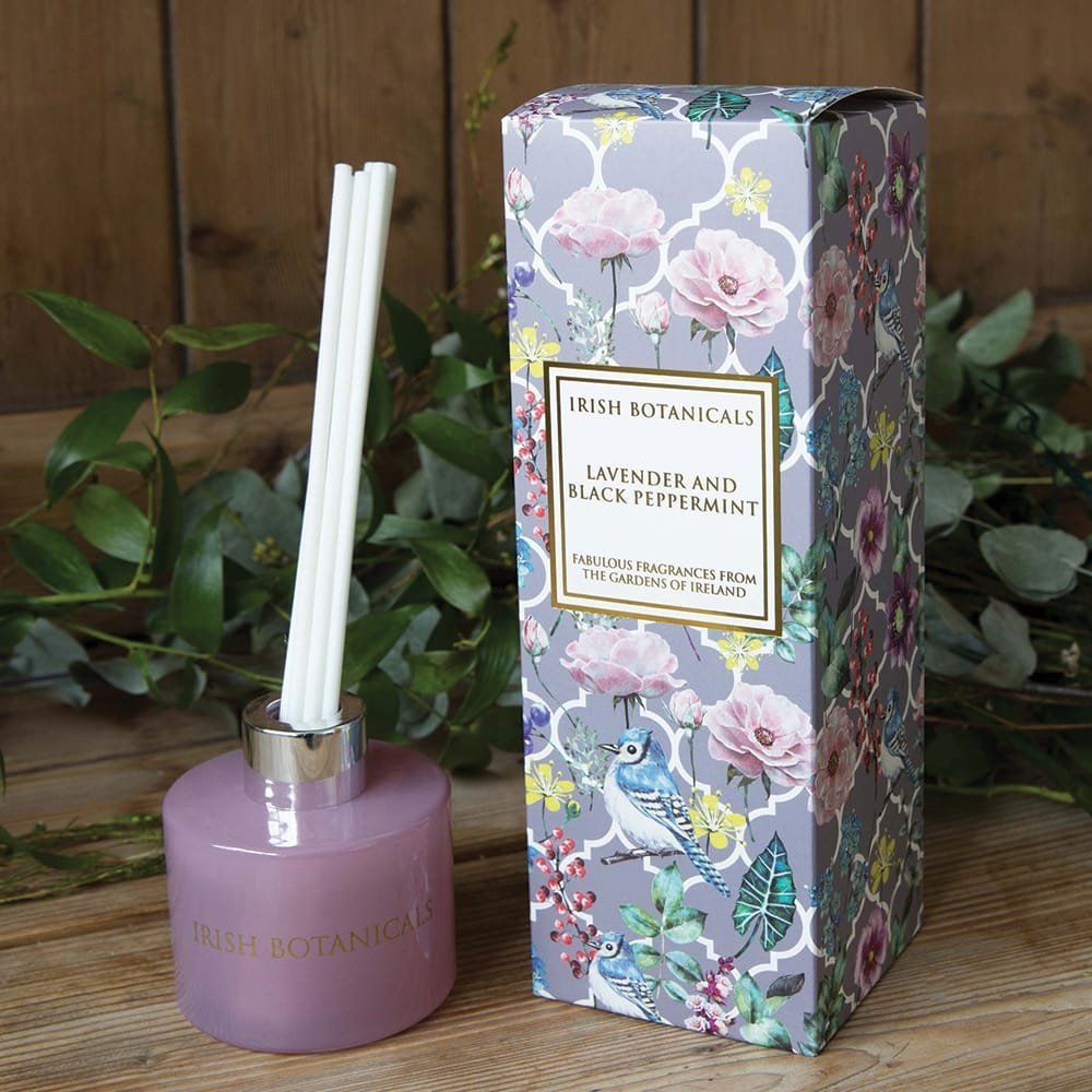 Rietdiffuser met witte rietjes, paarse fles en doos met bloemenpatroon.