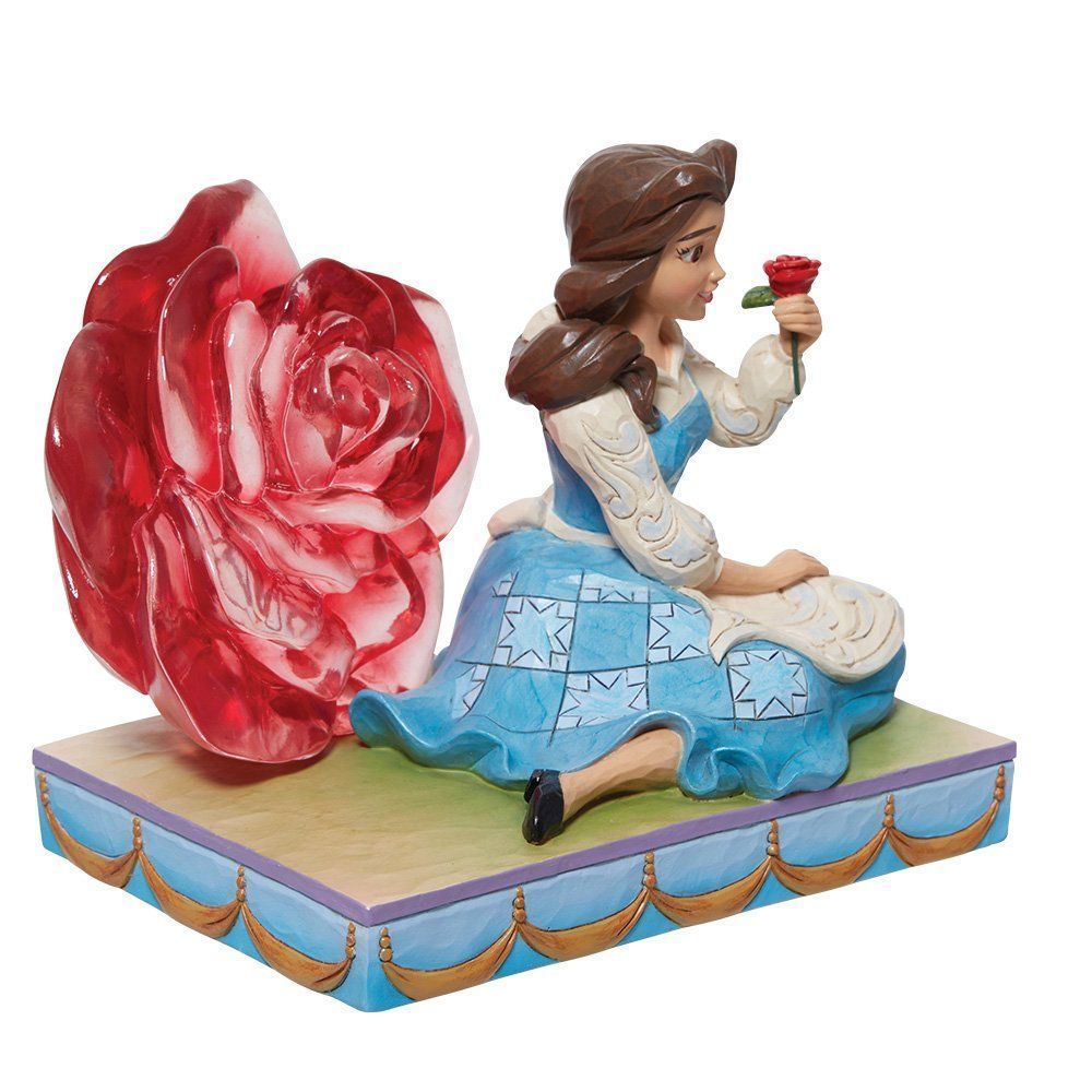 Een beeldje van Belle dat een roos vasthoudt, naast een grote rode roos, op een blauw gedetailleerde sokkel.