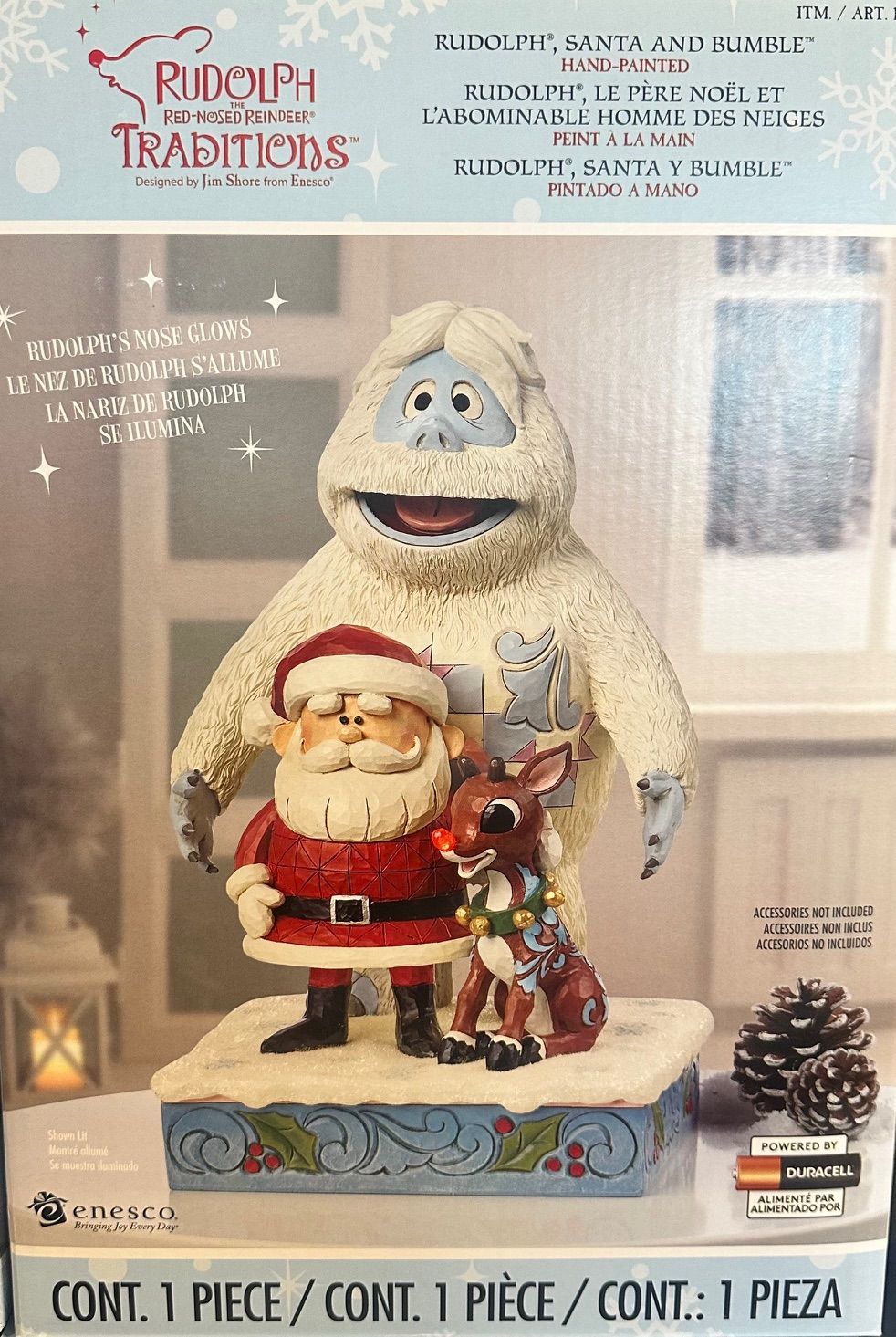 Kerstfiguren: de Kerstman, Rudolf, de Verschrikkelijke Sneeuwman en andere figuren op een besneeuwd platform, met kerstverlichting op de achtergrond.