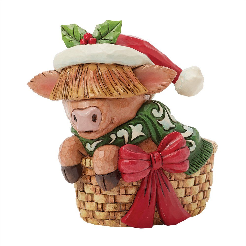Een koefiguurtje in een mandje met een kerstmuts, groene sjaal en rode strik.