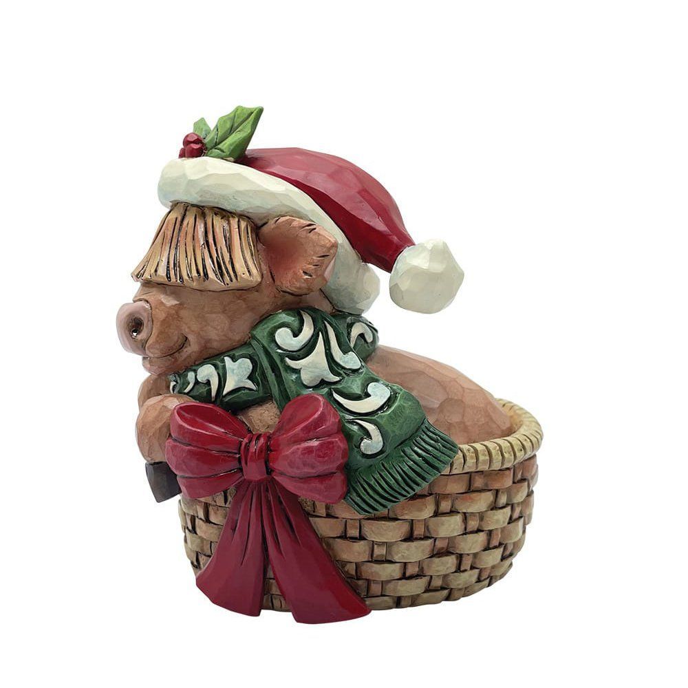 Een koefiguurtje in een mandje met een kerstmuts, groene sjaal en rode strik.