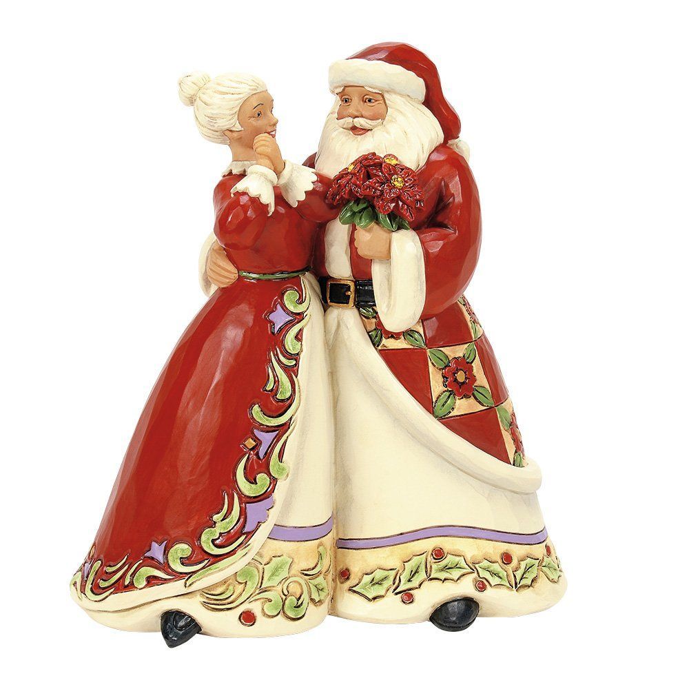 Een beeldje van de Kerstman en de Kerstvrouw in feestelijke rode en crèmekleurige jurken, die elkaar omhelzen en bloemen vasthouden.