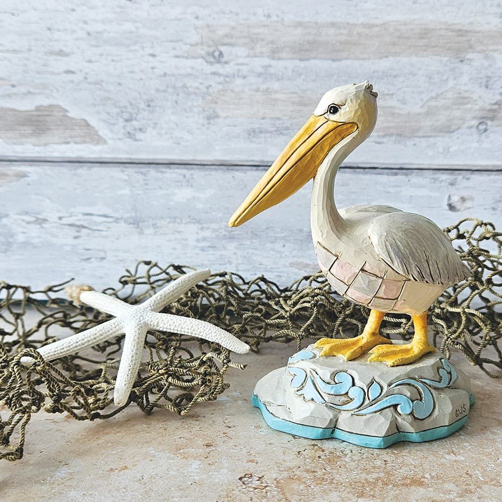 Een pelikaanbeeldje op een decoratieve sokkel met een zeester en een net in een kustlandschap.