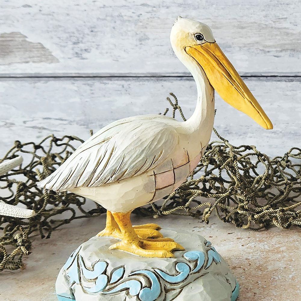 Beeld van een witte pelikaan met gele snavel en poten, op een decoratieve sokkel met blauwe accenten.