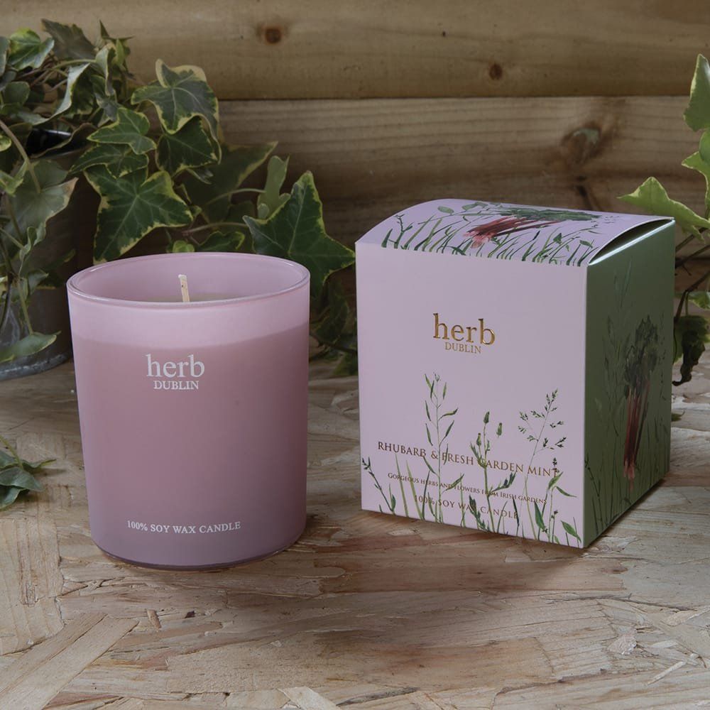 Roze geurkaars in een matglazen houder, met doosje, voor een groene achtergrond.
