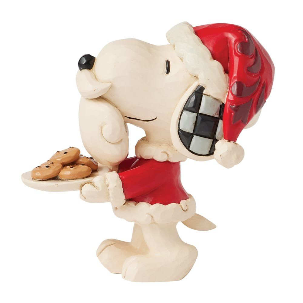 Snoopy in een kerstmanpak met een bord koekjes. Beige hond met rode muts en jas, lachend.