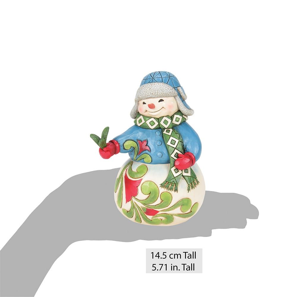 Sneeuwpopfiguurtje met een blauwe muts, jas, groene sjaal, rode wanten en een versierde voet met een bloemenmotief.