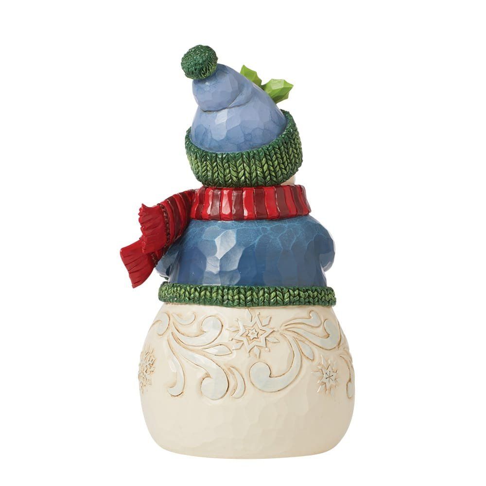 Sneeuwpopfiguurtje met een blauwe muts, rode sjaal en groene trui, op een gedetailleerde crèmekleurige sokkel.