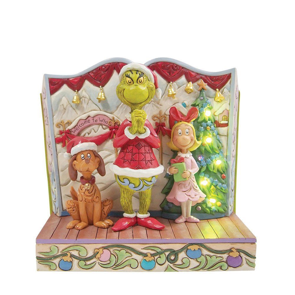 Een kerst-Grinch-beeldje met de Grinch, Max en Cindy Lou Who op een podium met een verlichte kerstboom.