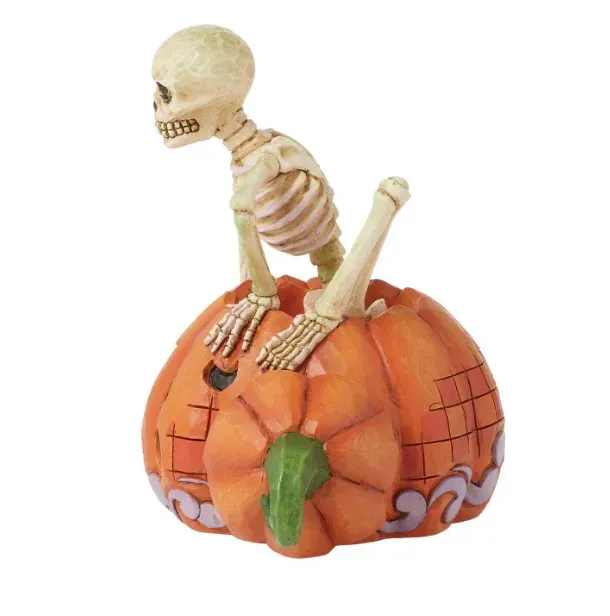 Een skelet dat uit een uitgeholde oranje pompoen tevoorschijn komt.